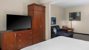 A hotel room with a bed, a wooden wardrobe with a flat-screen TV, a sofa, and a small table with a lamp.