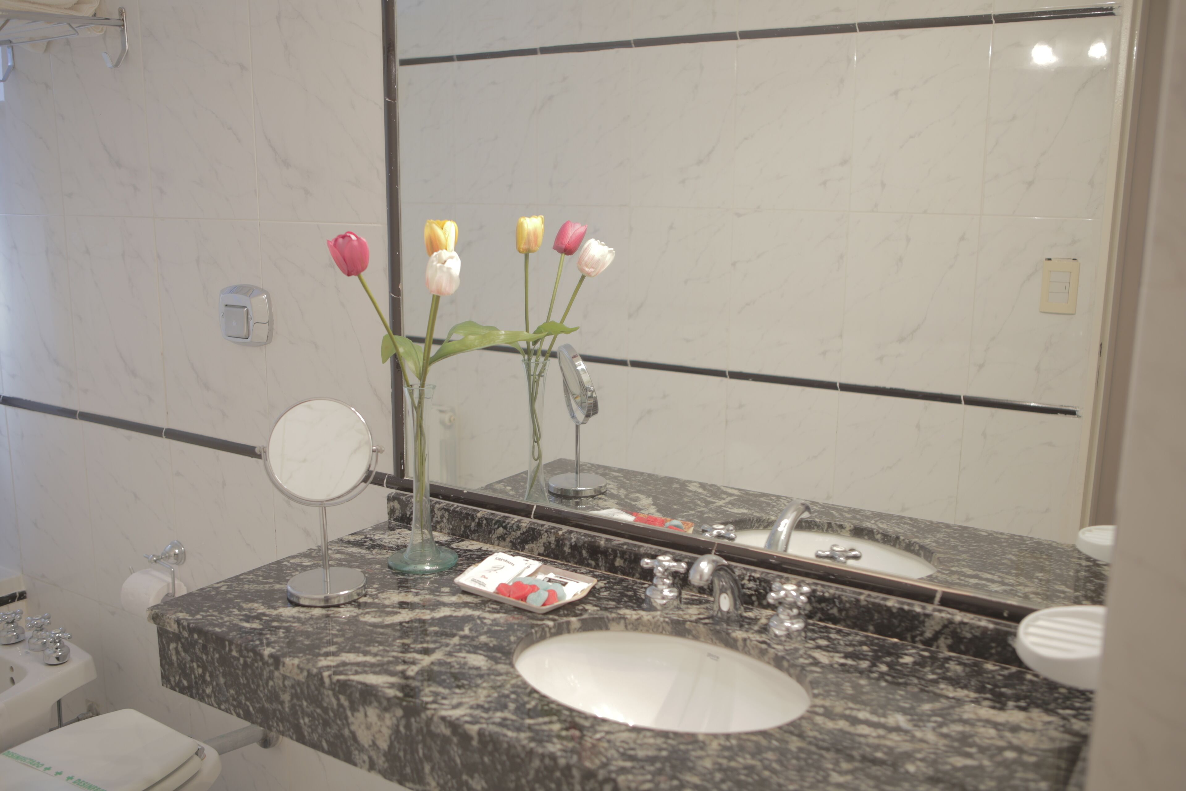 Un baño con lavamanos de mármol, un espejo y un florero con flores.