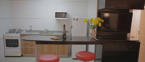 A modern kitchen with a central island, two red bar stools, a microwave, a refrigerator, and a stove.
