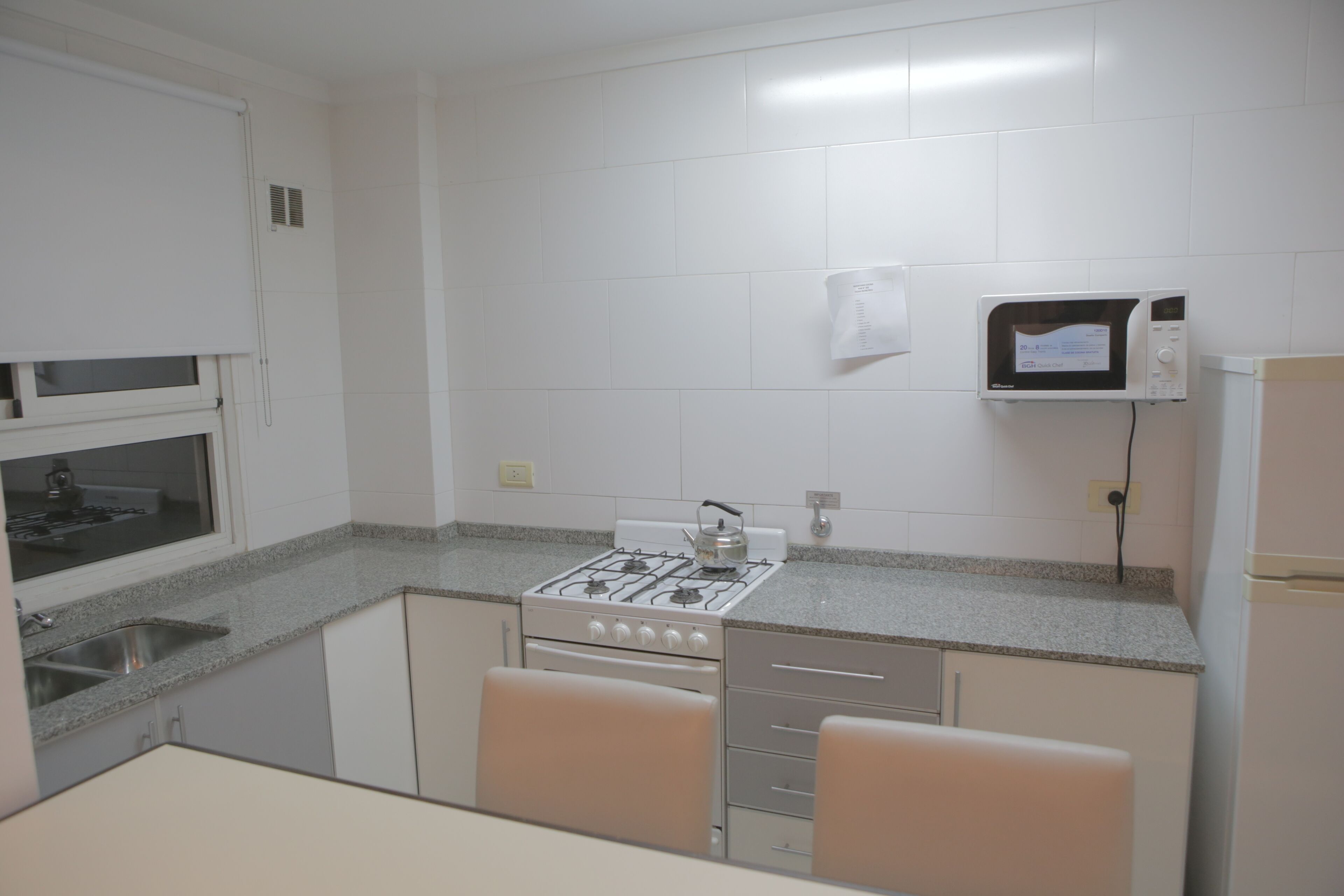Una cocina con armarios blancos, estufa a gas, microondas y refrigerador.