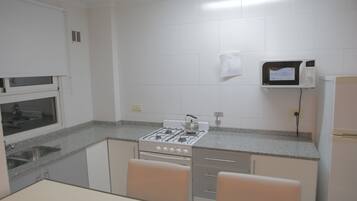 Una cocina con armarios blancos, estufa a gas, microondas y refrigerador.