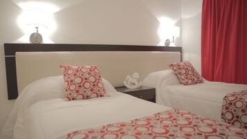 A hotel room with two beds, each with a red and white patterned bedspread, a nightstand with a lamp, and a red curtain.