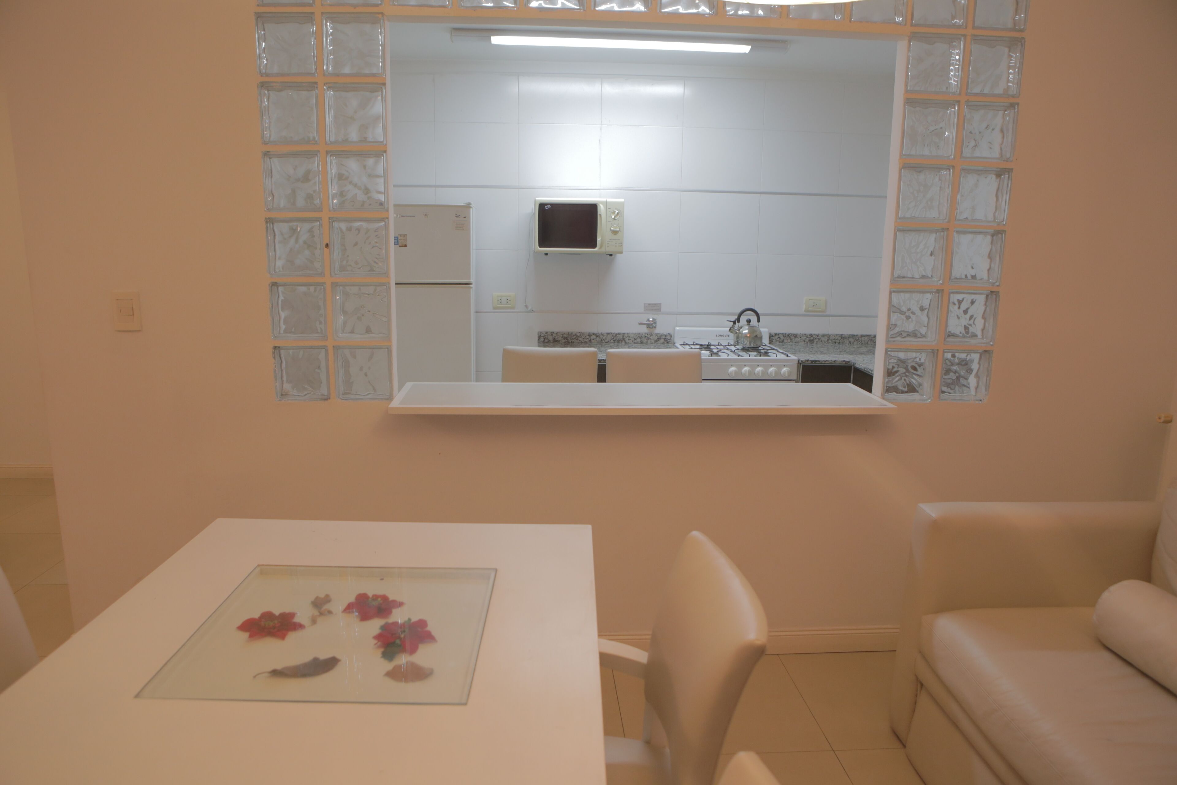 A room with a dining table, a chair, a sofa, and a kitchen area visible through a glass partition.