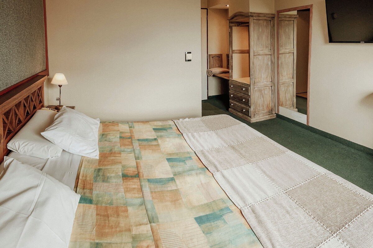 A bedroom with a bed, a nightstand, a lamp, a quilt, a wardrobe, and a mirror.