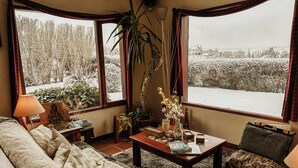 Ein gemütliches Wohnzimmer mit einer Couch, einem Couchtisch und Blick auf eine verschneite Landschaft durch große Fenster.