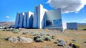 Ein modernes Gebäude mit markantem architektonischen Design, das mehrere weiße und blaue Strukturen in einer natürlichen Landschaft mit Bergen im Hintergrund zeigt.
