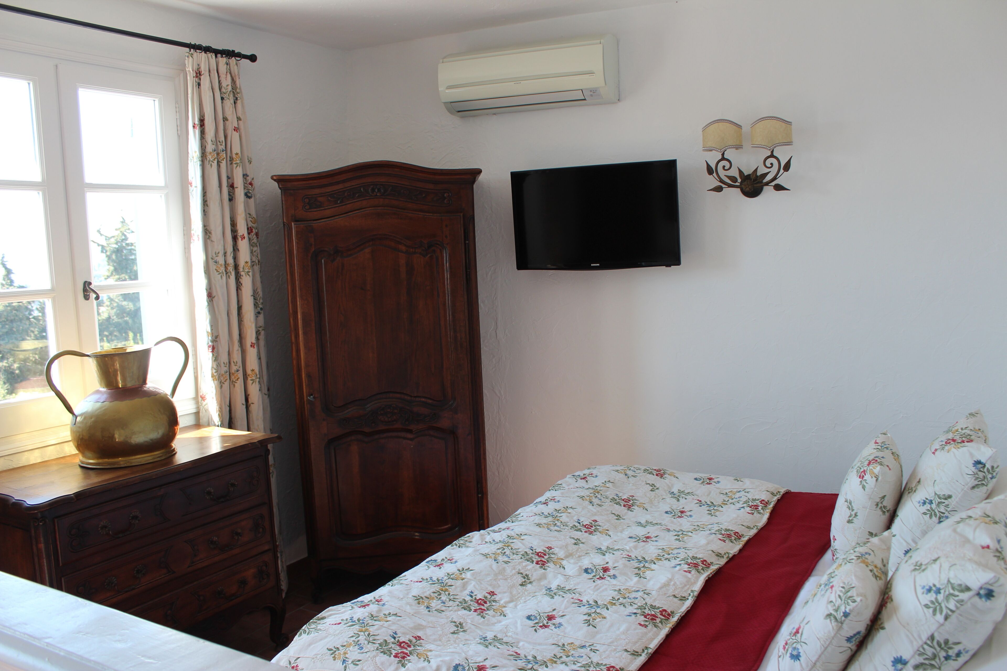 Ein Schlafzimmer mit einem Bett, einem Holzschrank, einem Fernseher und einem Fenster mit Vorhängen.