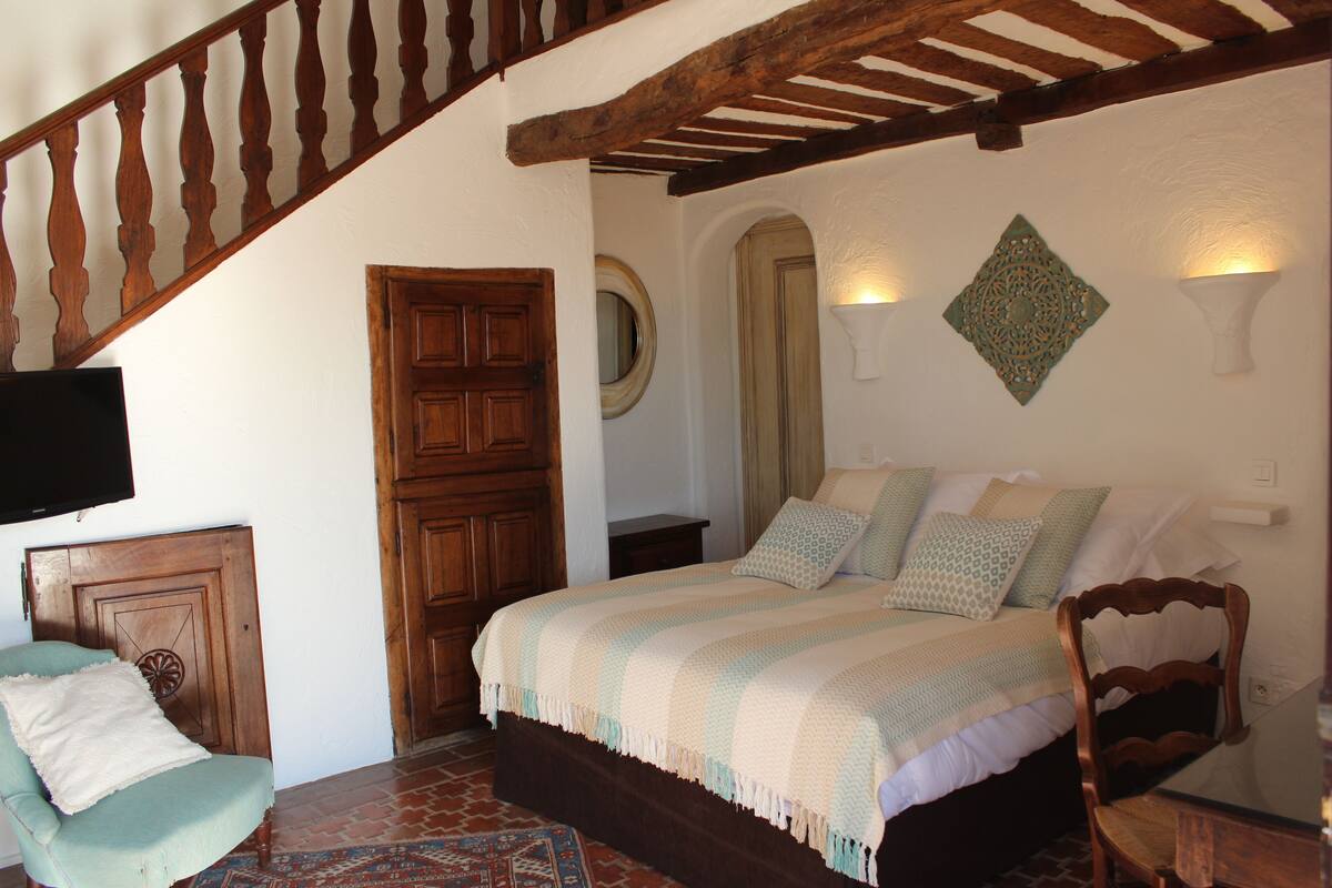 A bedroom with a wooden bed, a chair, a television, and a staircase.