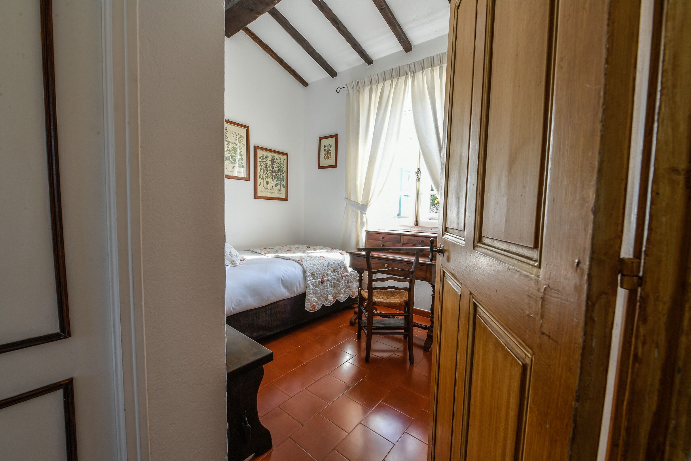 Ein Schlafzimmer mit einem Bett, einem Schreibtisch und einem Stuhl. An den Wänden hängen gerahmte Bilder.