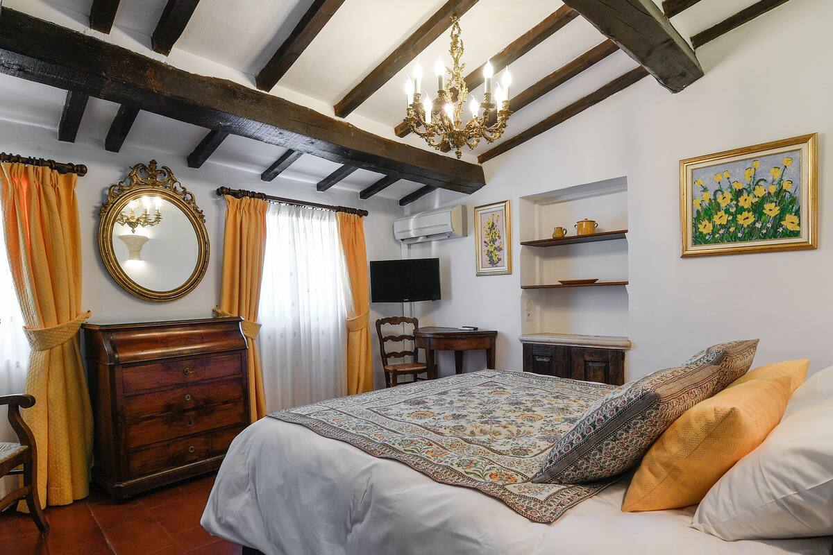 A bedroom with a bed, wooden dresser, and a chandelier.
