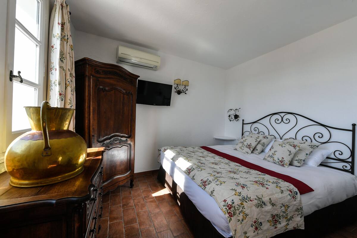 A bedroom with a bed, a wooden wardrobe, a television, and a window with curtains.
