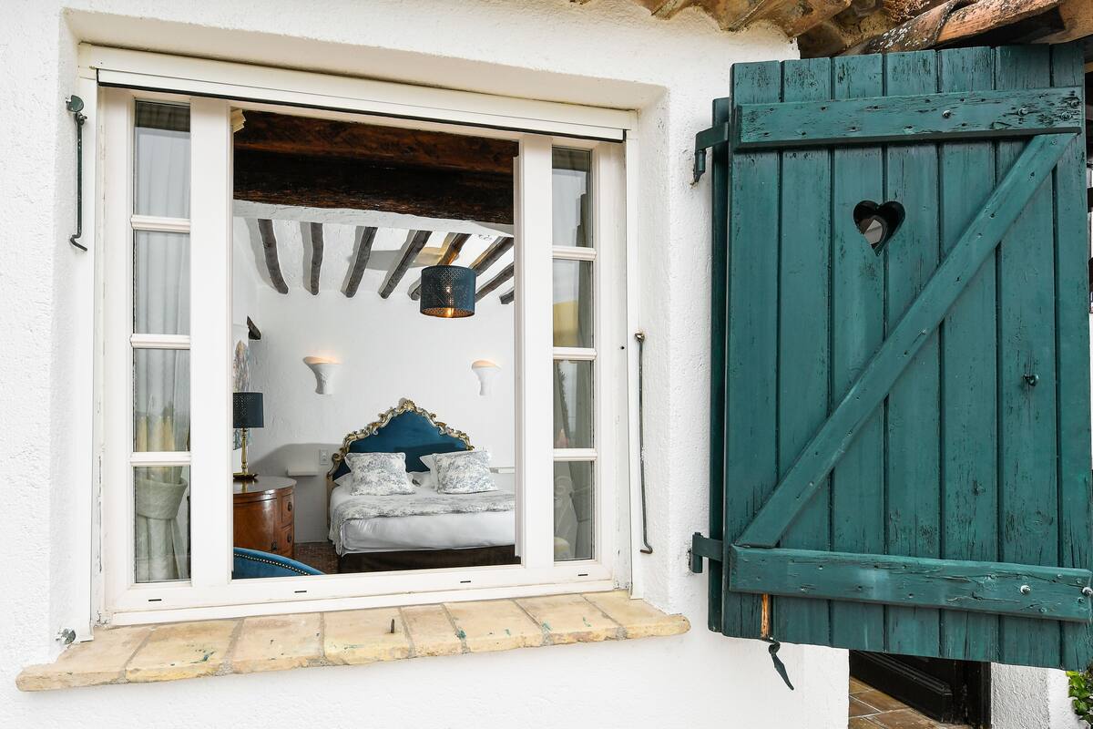 A room with a bed, a window, and a wooden door with a heart-shaped cutout.