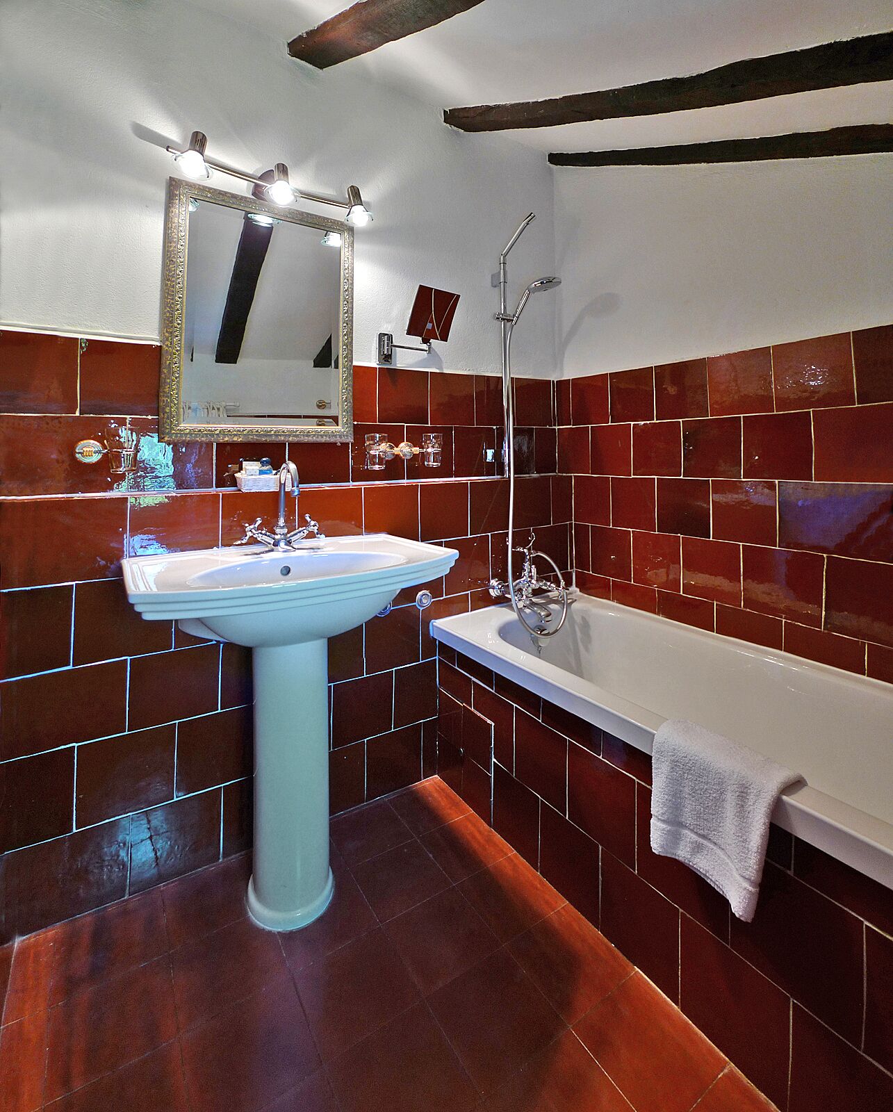 A bathroom with a pedestal sink, a bathtub, and a mirror with lights.