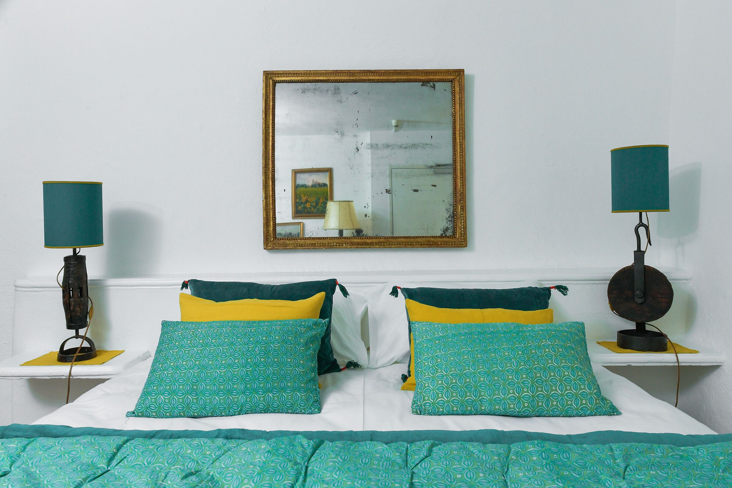 A neatly made bed with patterned pillows, a bedside lamp, and a mirror on the wall.