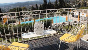 Un balcón con vistas a una piscina, barandillas de metal blanco y sillas amarillas.