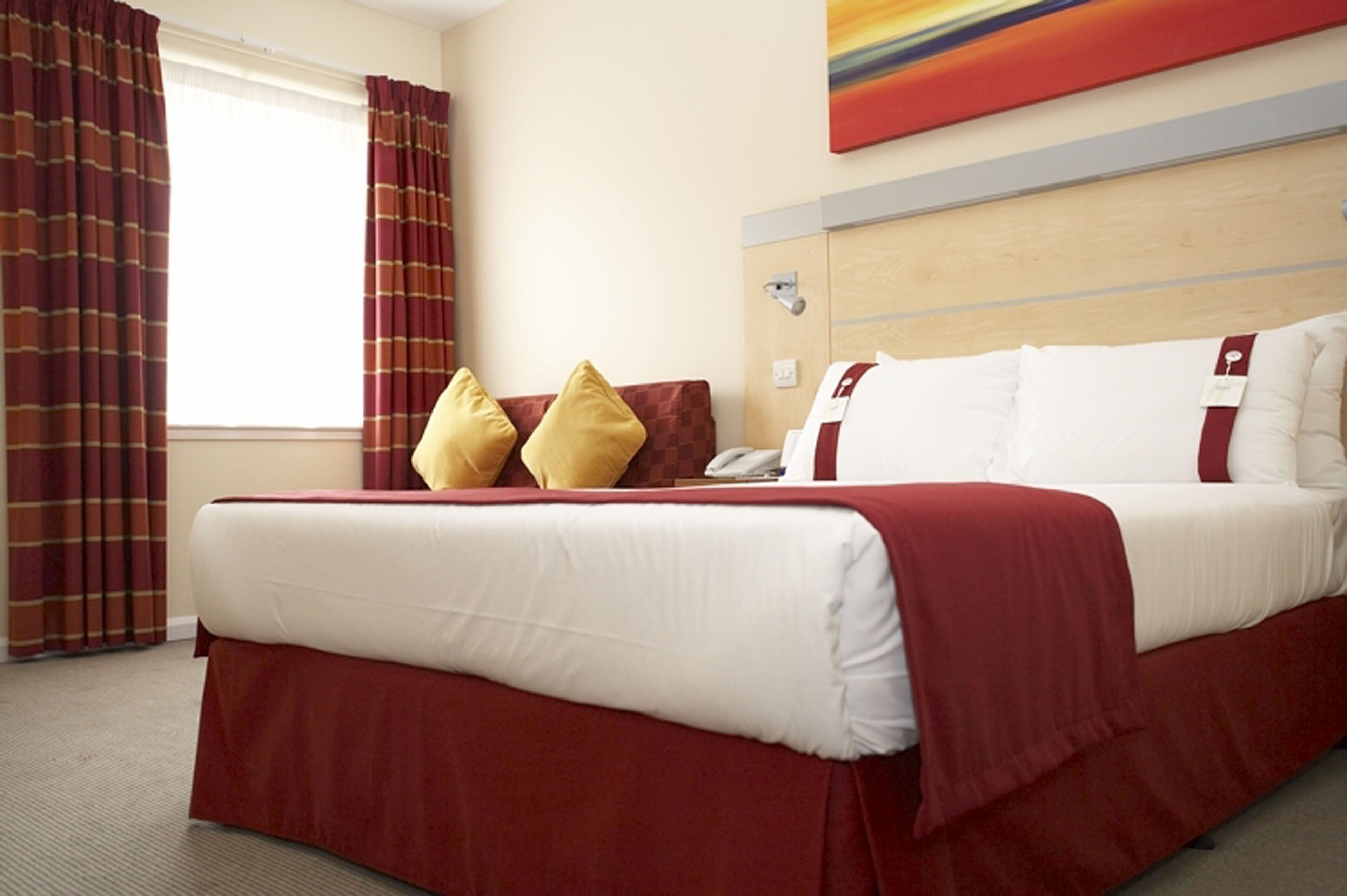 Une chambre d’hôtel avec un lit, des oreillers, un téléphone et une fenêtre avec des rideaux.