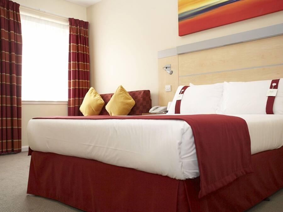 A hotel room with a bed, pillows, a telephone, and a window with curtains.