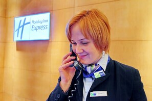 Une personne portant un badge nominatif et un uniforme orné d’un logo, se tenant devant une enseigne indiquant « Holiday Inn Express ».