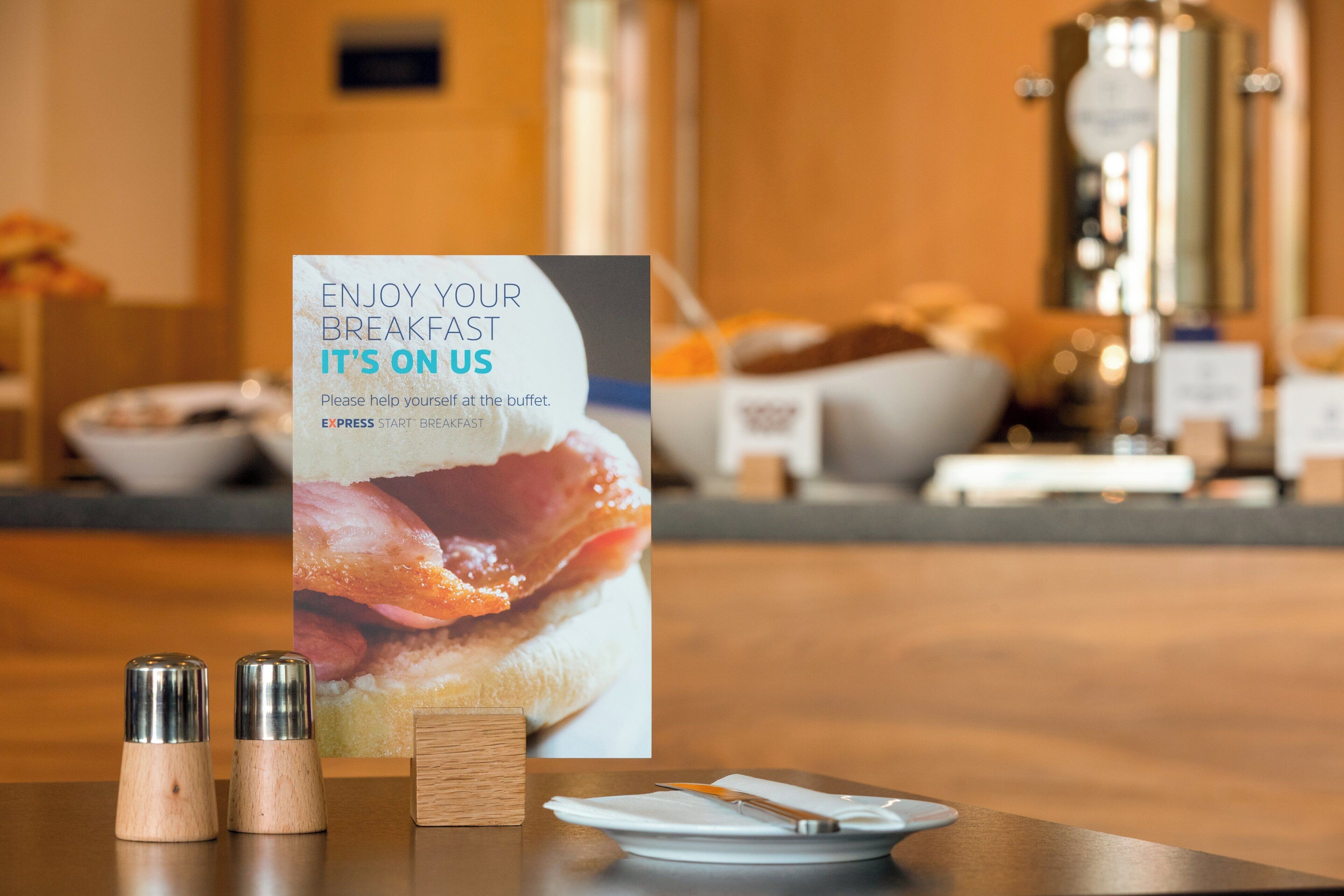 A breakfast buffet setup with a sign, salt and pepper shakers, a napkin, and a plate.