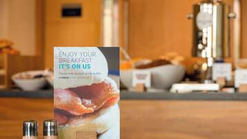 A breakfast buffet setup with a sign, salt and pepper shakers, a napkin, and a plate.