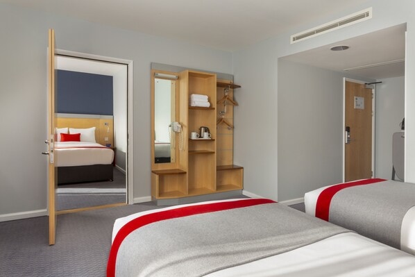 Une chambre d’hôtel avec deux lits, une armoire, un miroir et une porte donnant sur une autre pièce.