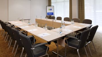 A conference room with a long table, chairs, water bottles, and a projector screen.