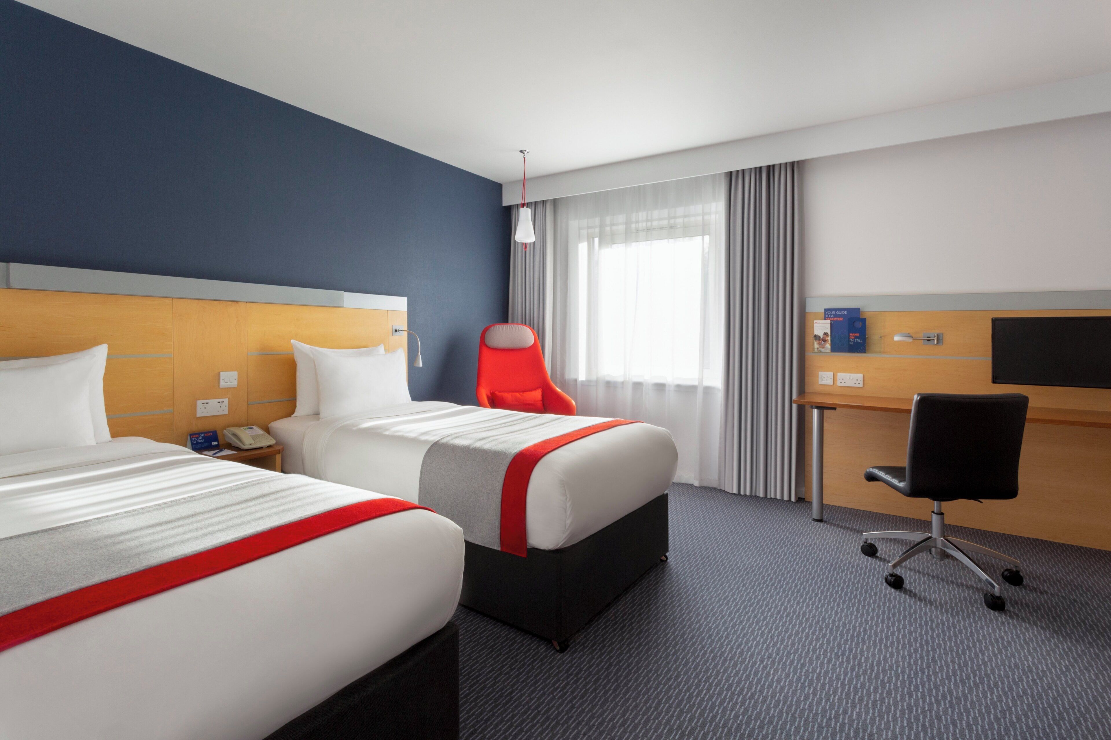 A hotel room with two beds, a desk, a chair, and a television.