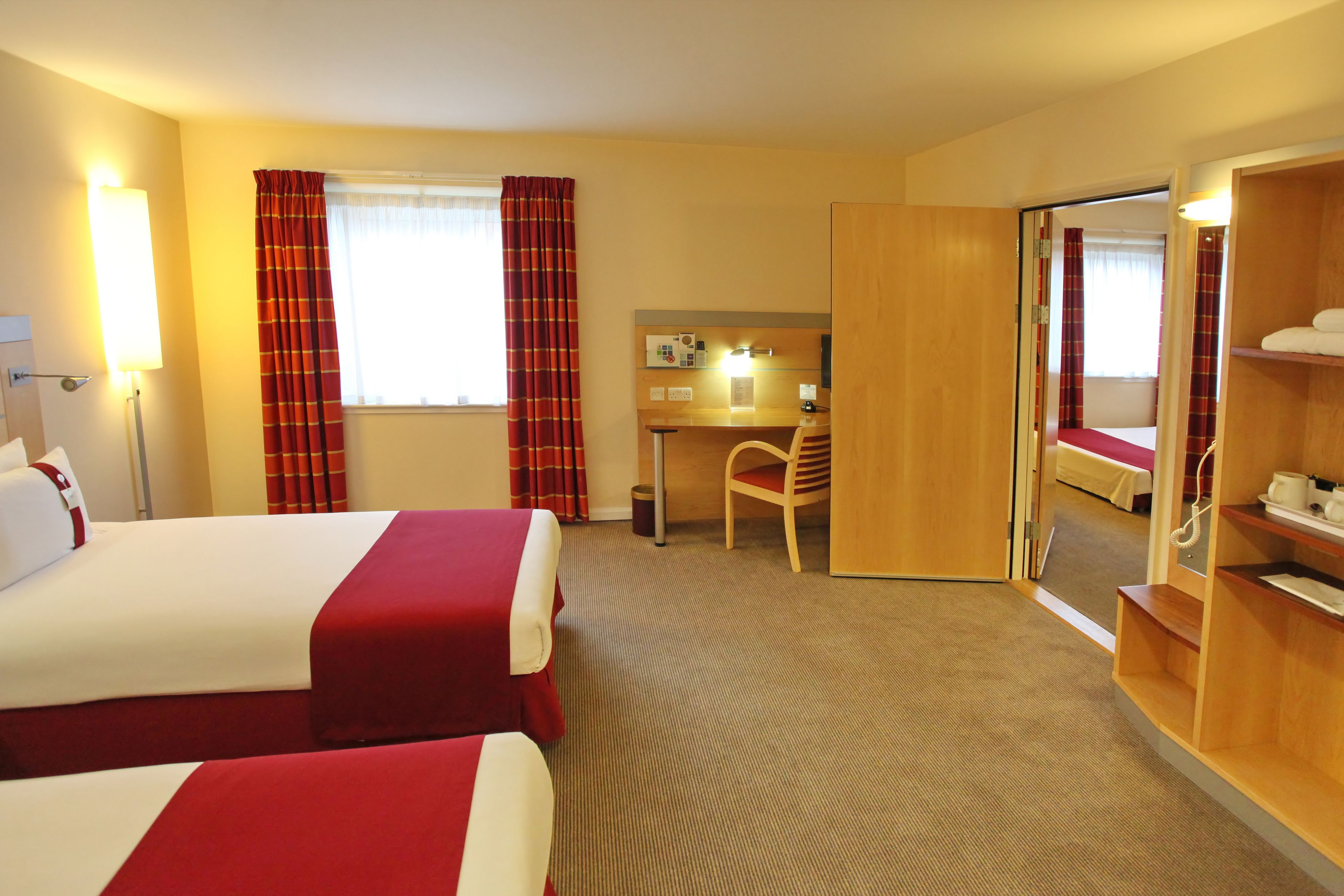 Ein Hotelzimmer mit zwei Betten, einem Schreibtisch, einem Stuhl und einem Spiegel.