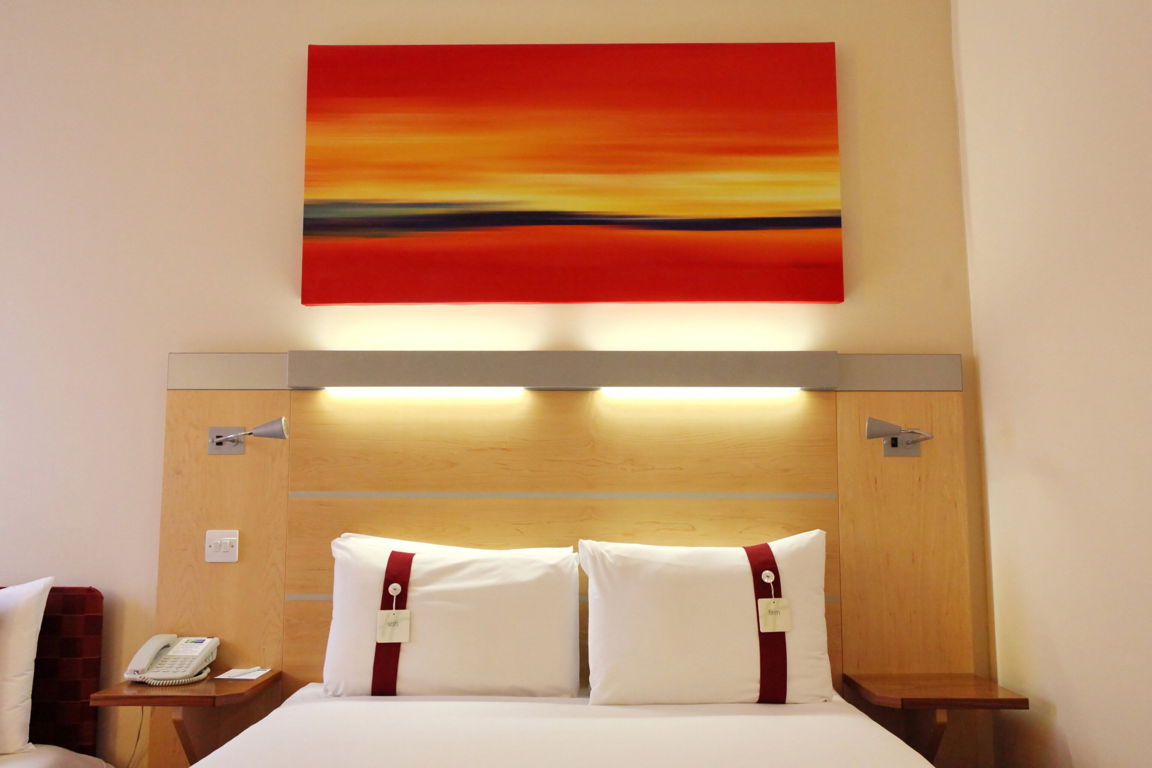 A hotel room with a bed, a nightstand, a telephone, and a painting on the wall.