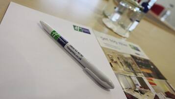 A white notepad with a pen on top, a glass of water, and a blurred background with a poster.