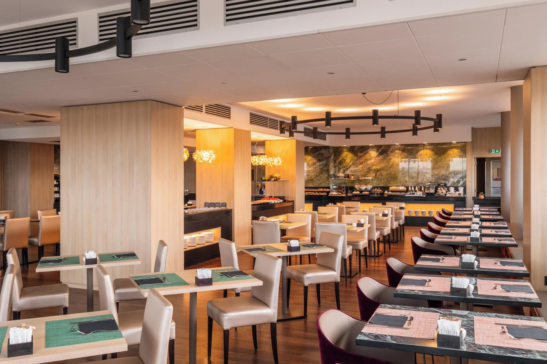 A restaurant with multiple dining tables and chairs, a buffet area, and a large mural on the wall.