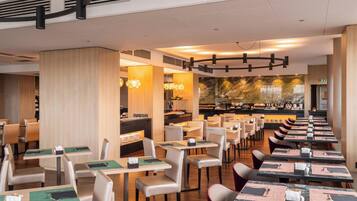A restaurant with multiple dining tables and chairs, a buffet area, and a large mural on the wall.