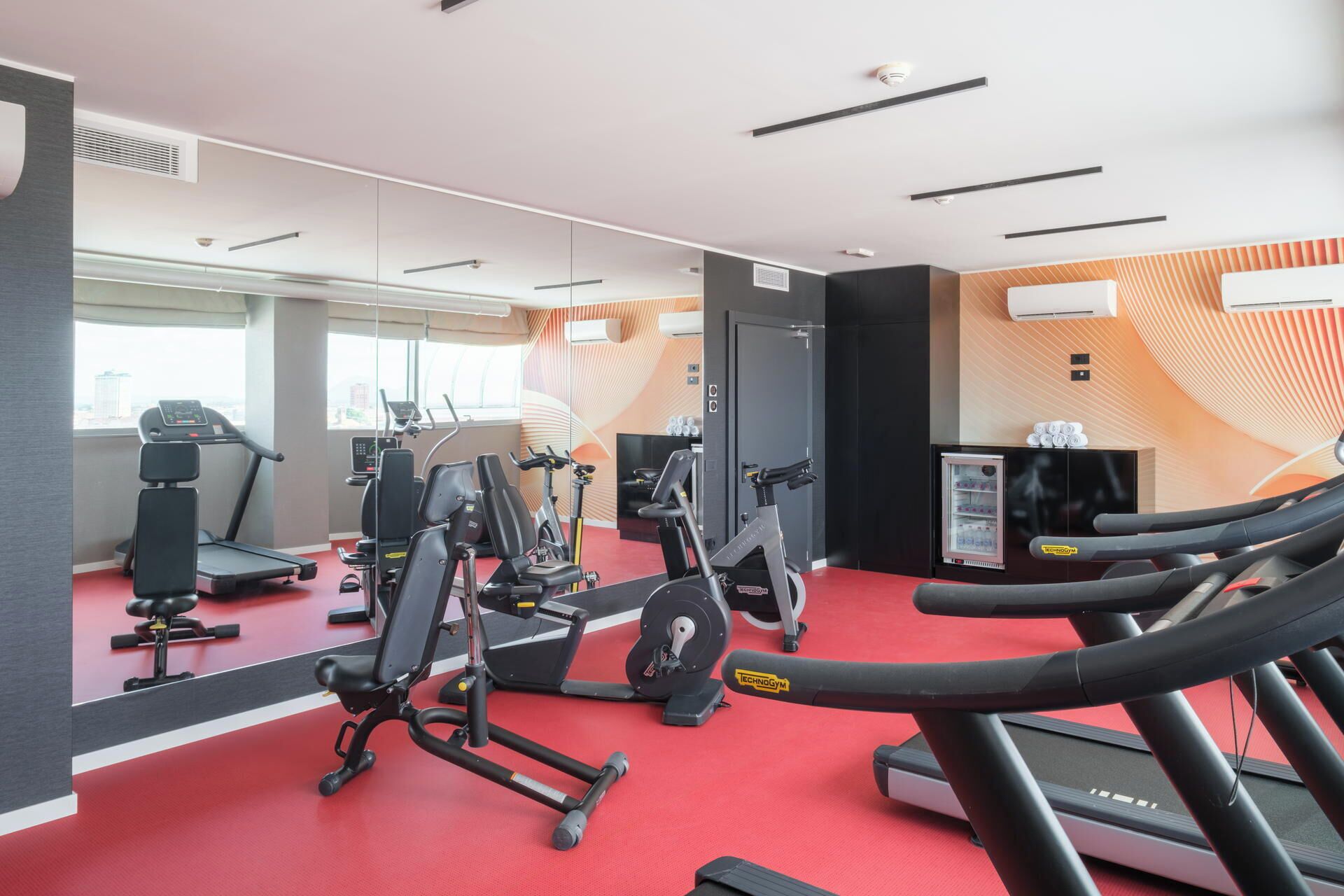 A gym with exercise equipment, a treadmill, and a mirrored wall.