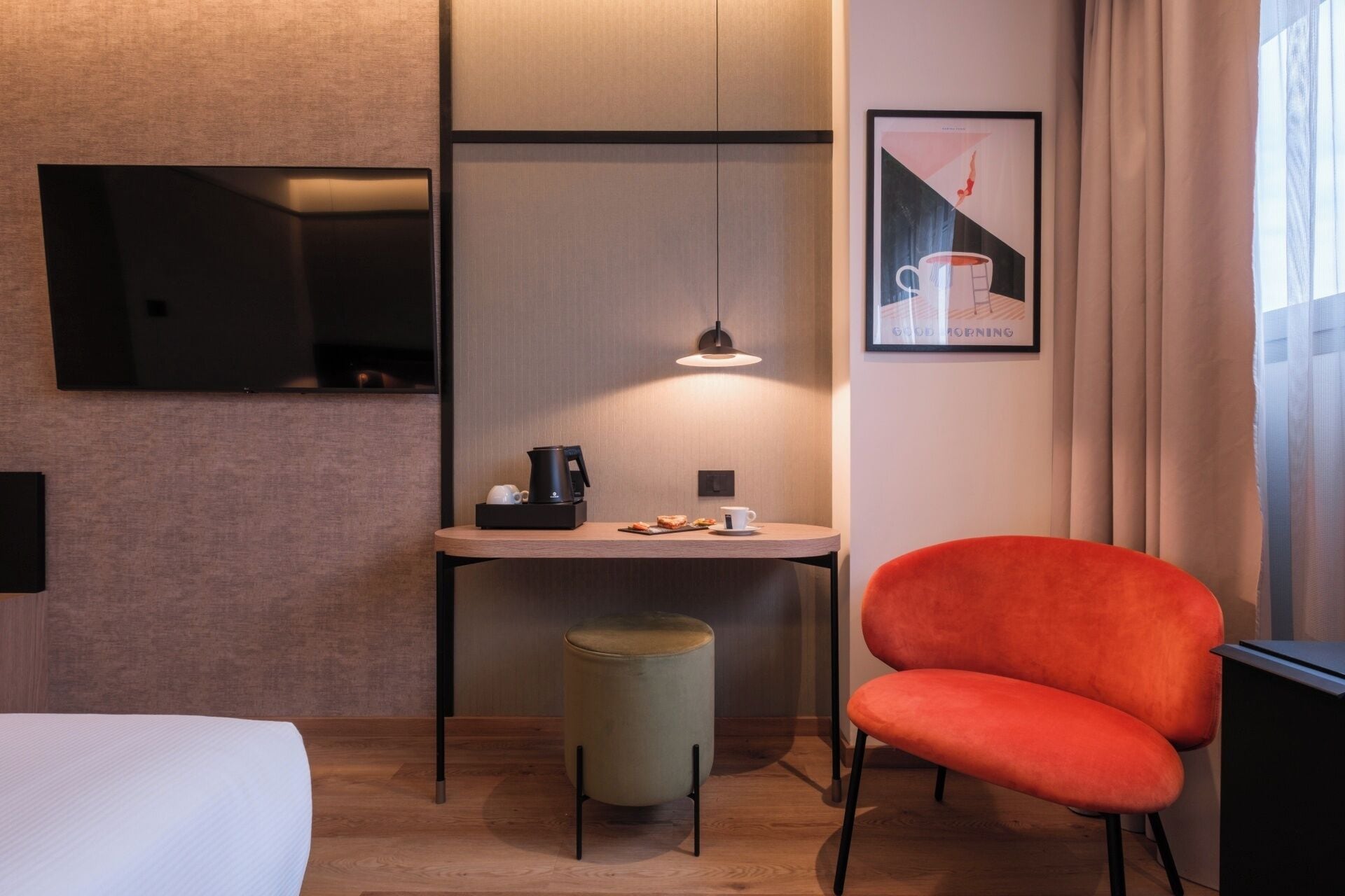 A hotel room with a bed, a small round table with a coffee maker, a chair, a television, and a framed picture on the wall.