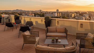 Eine Dachterrasse mit Korbmöbeln, einem Tisch und Topfpflanzen.