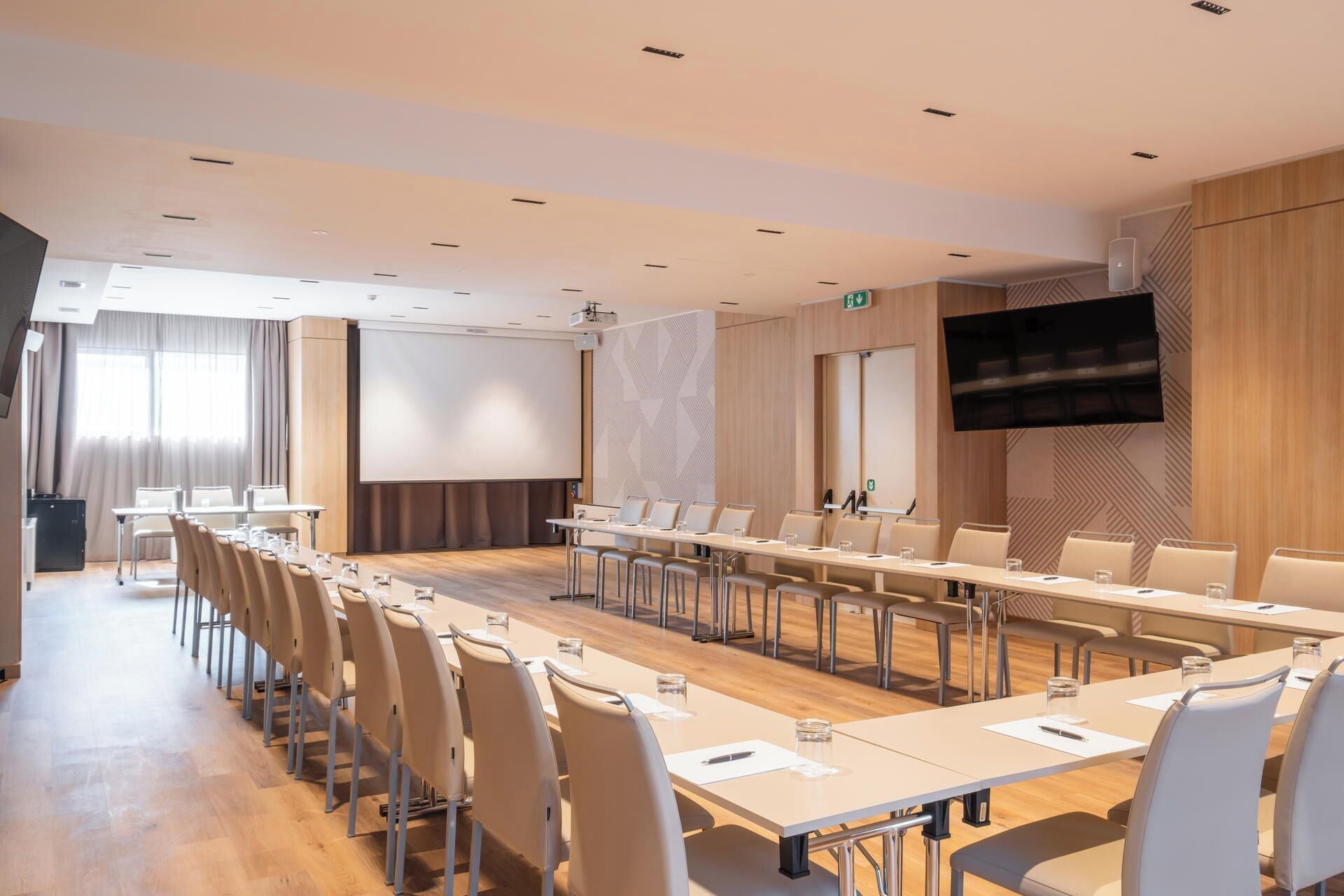 A conference room with a long table, chairs, a projector screen, a TV, and a wooden panel wall.