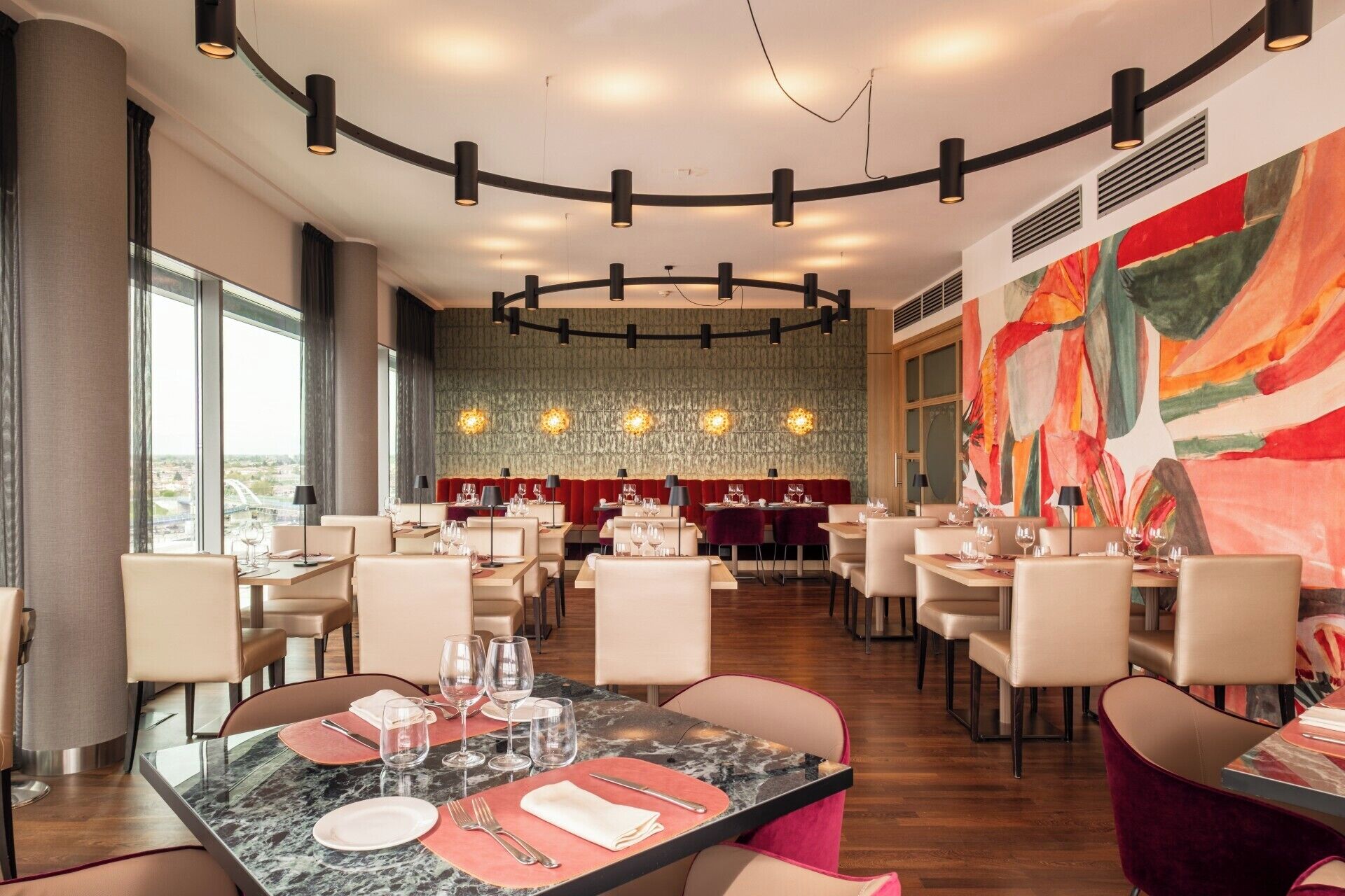 Un espace repas moderne avec des tables rondes, des chaises et un grand tableau abstrait accroché au mur.