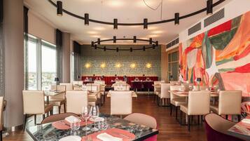 Un espace repas moderne avec des tables rondes, des chaises et un grand tableau abstrait accroché au mur.