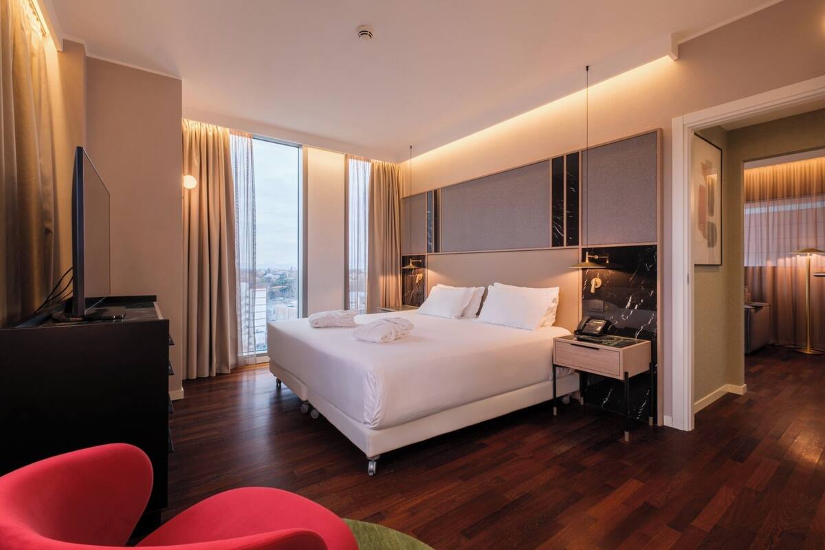 A modern hotel room with a large bed, a desk, and a chair.
