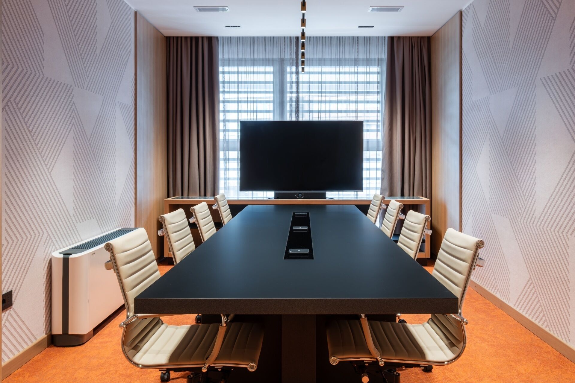 A conference room with a large table, chairs, a flat-screen TV, and a window with curtains.