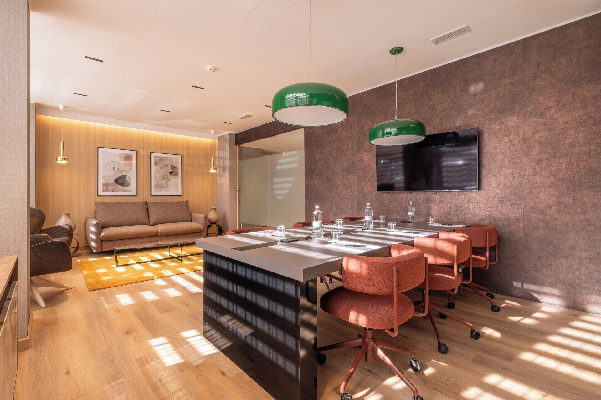 Una habitación de hotel moderna con suelo de madera, un sofá, una mesa de comedor con sillas y un televisor de pantalla plana montado en la pared.
