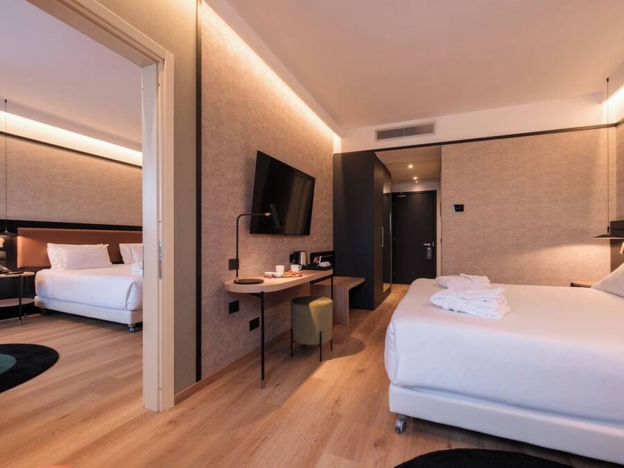 Habitación de hotel con dos camas, un escritorio, un televisor y la puerta del baño.