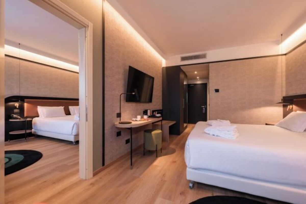 A hotel room with two beds, a desk, a flat-screen TV, and a mirror.