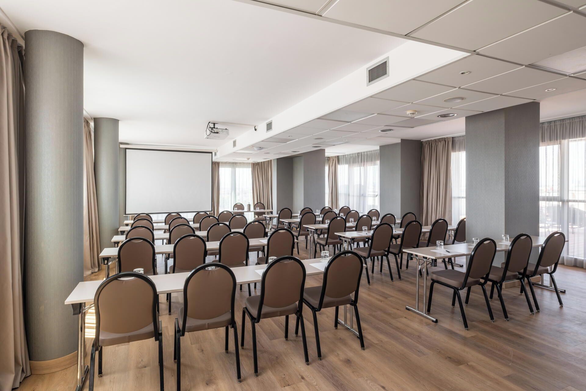 A conference room with a large screen, multiple tables, and chairs arranged for meetings.