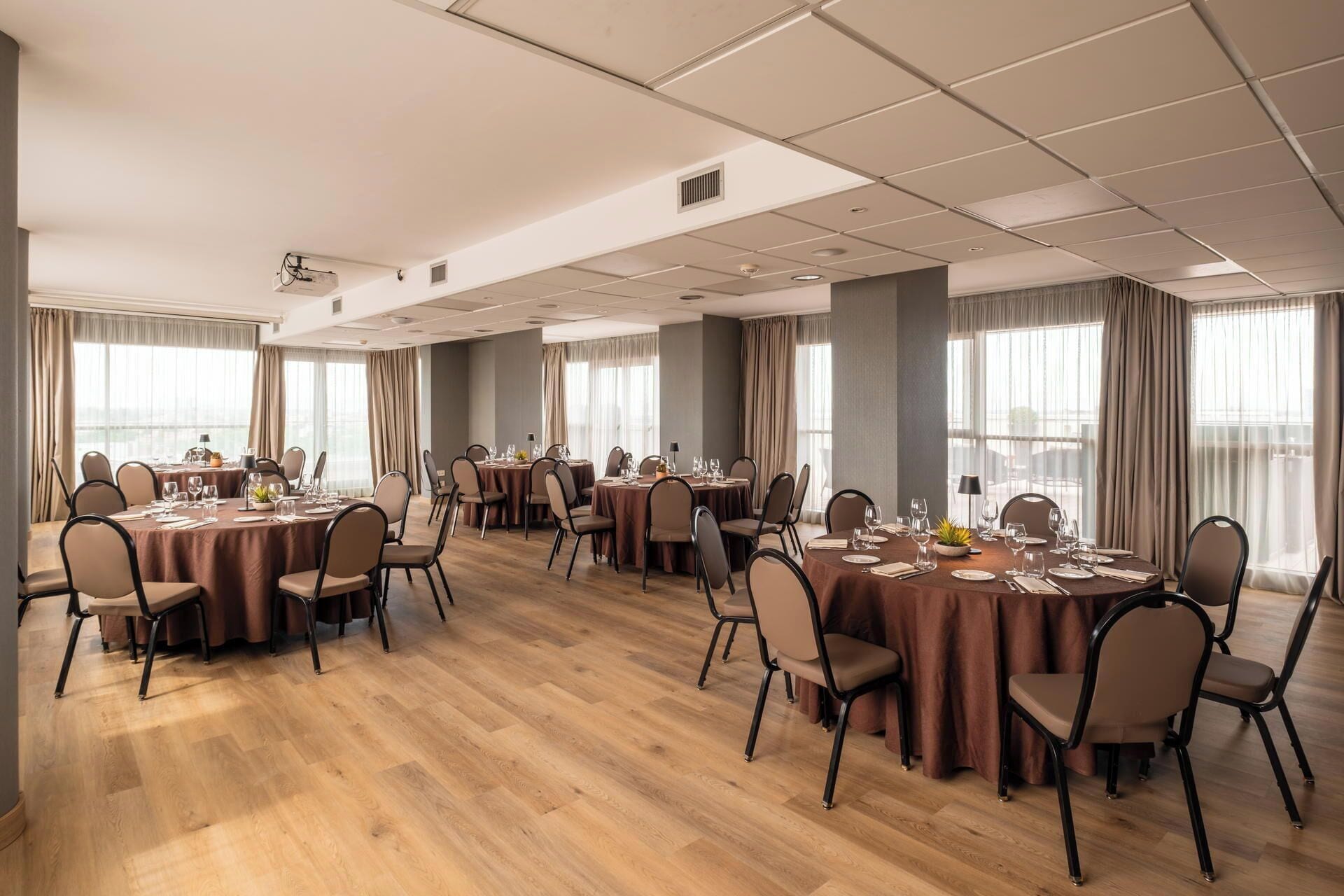 A conference room with multiple round tables, chairs, and a view of the city through large windows.