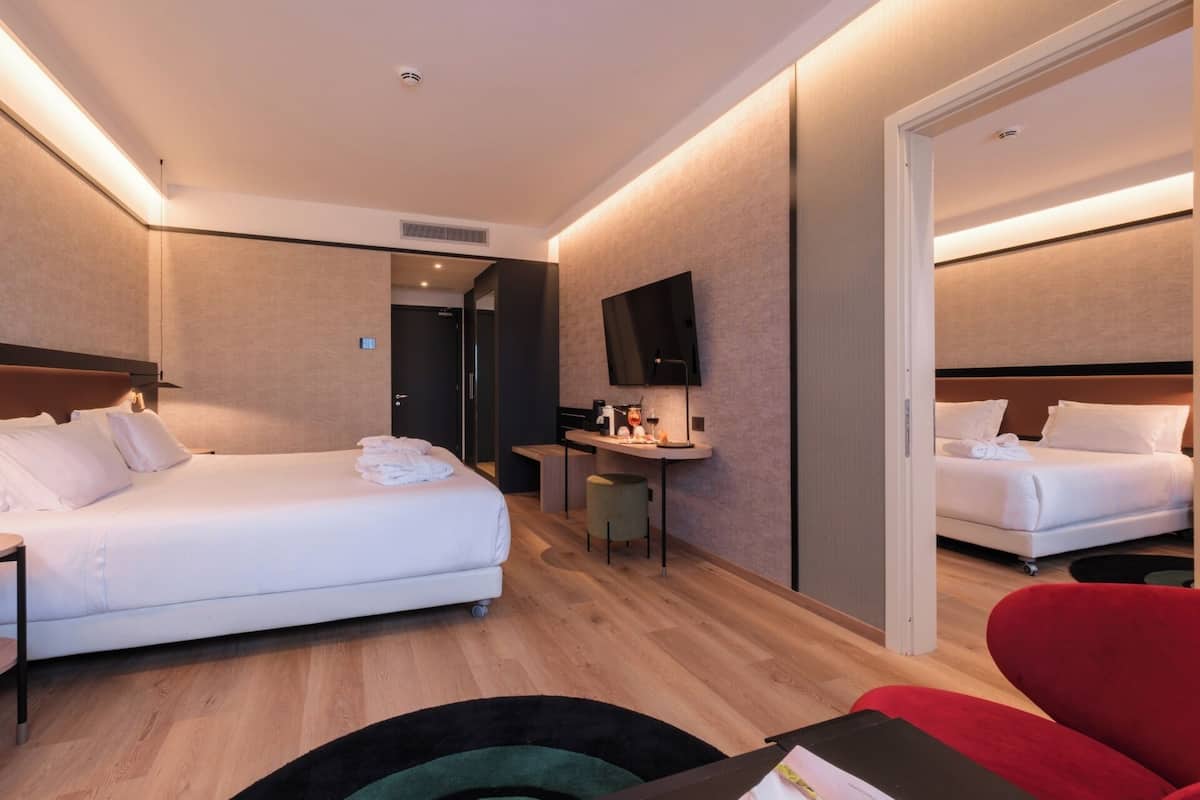 A hotel room with two beds, a desk, a TV, and a mirror.