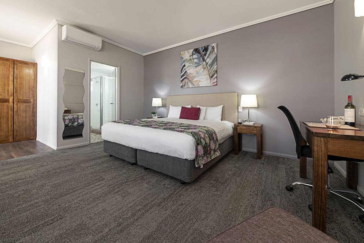 Una habitación de hotel con una cama, mesitas de noche, un escritorio y una silla.