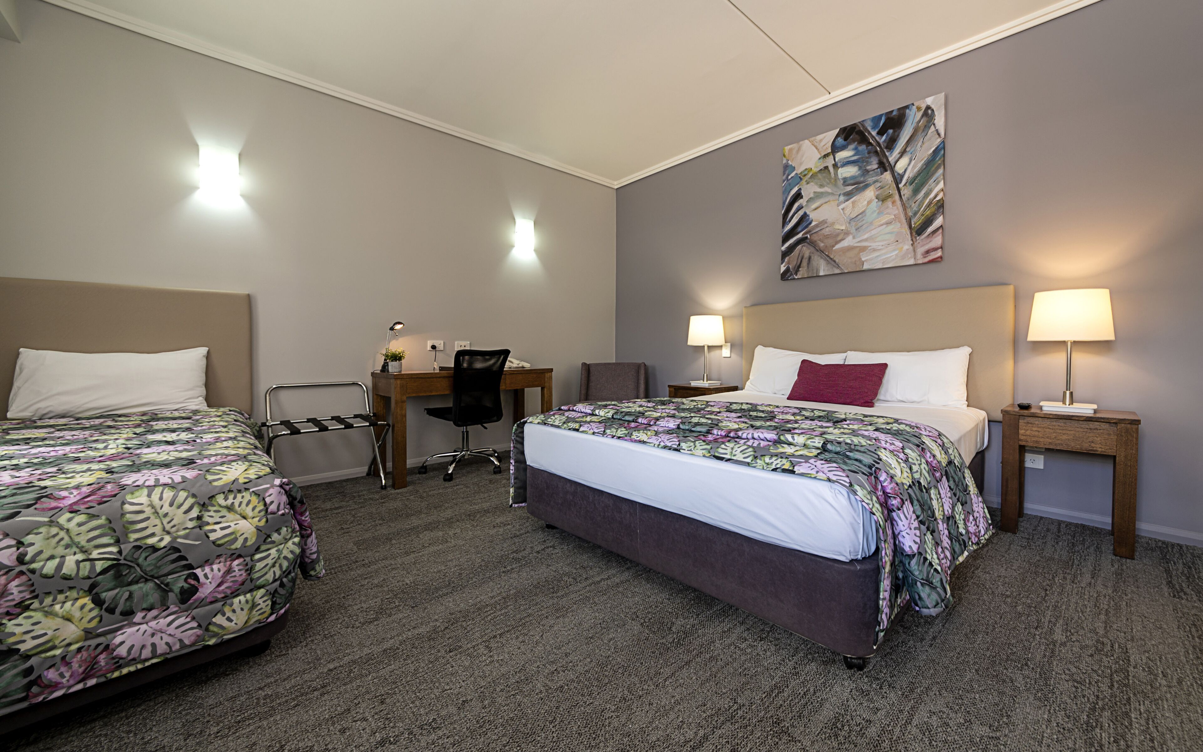 Une chambre d’hôtel avec deux lits, un bureau, une chaise et un tableau au mur.