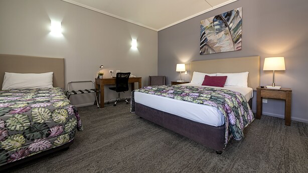 A hotel room with two beds, a desk, a chair, and a painting on the wall.
