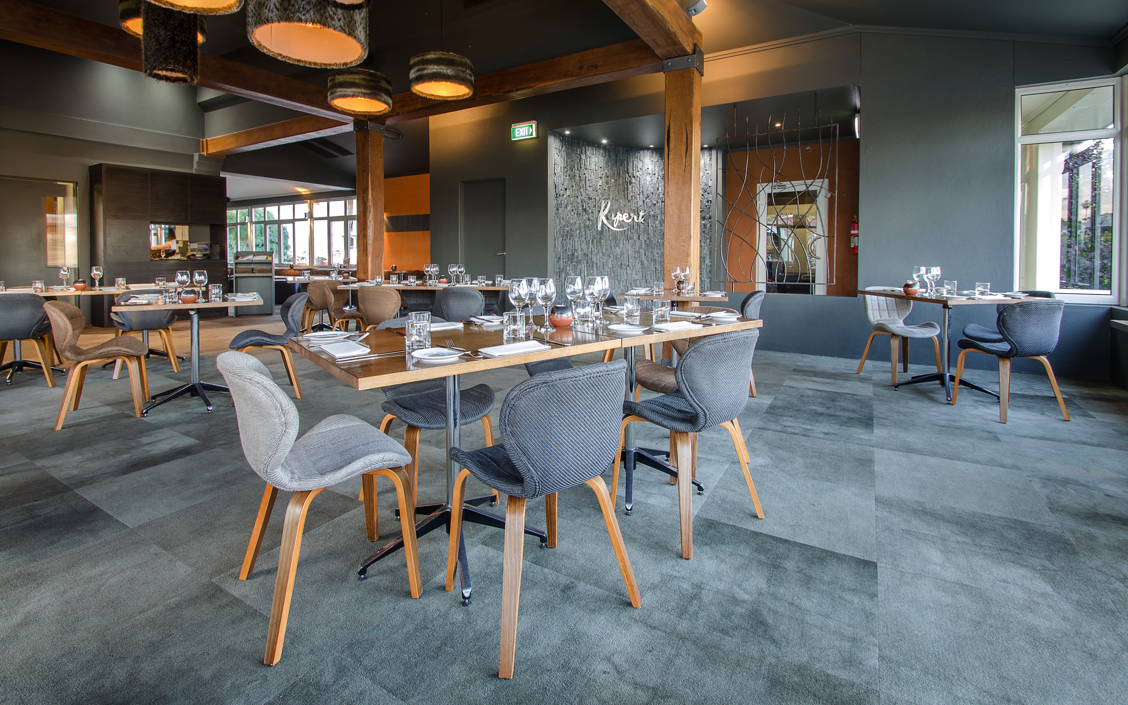 A modern restaurant with multiple dining tables and chairs, featuring a mix of wooden and upholstered seating.